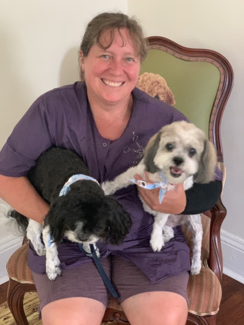 The groomer seated holding two small freshly groomed dogs